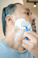 Asian man shaving beard with razor.