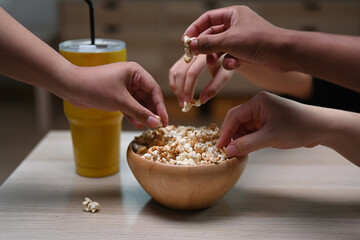 Group of young friends eating popcorn in living room.