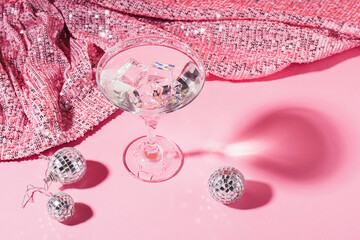 Martini with ice in an elegant glass of disco balls on a shiny pink background. Fashionable bright...