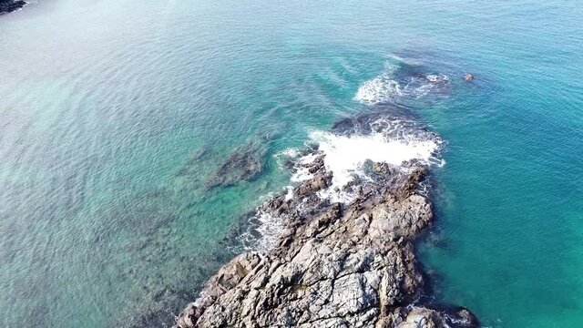 Overhead aerial drone of rocky outcrop, blue ocean and waves in Maitai Bay, Karikari Peninsula, Northland, New Zealand Aotearoa