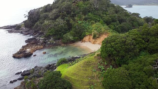 Rising aerial drone of green rocky outcrop in the rain on Maitai Bay in the rain, Karikari Peninsula, Northland, New Zealand Aotearoa