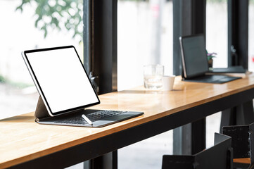 Mockup blank screen tablet with keyboard on wooden counter table in co-workspace.