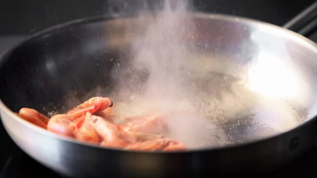 Cook tosses shrimps on grill. Closeup of king prawns frying in a pan. Chef frying royal shrimps on a hot pan. Macro sea food preparation.