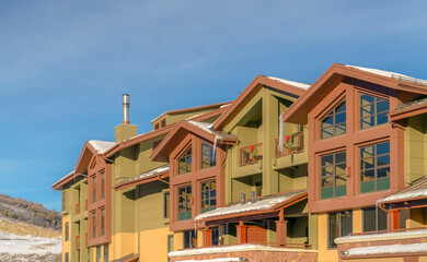 Homes with large glass windows and snowy roofs against frosty hill and blue sky