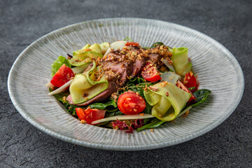 Hearty salad with duck fillet, tomatoes, zucchini and spinach. Diet food. Ready menu for the restaurant. Neutral gray blue textured background