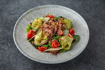 Hearty salad with duck fillet, tomatoes, zucchini and spinach. Diet food. Ready menu for the restaurant. Neutral gray blue textured background