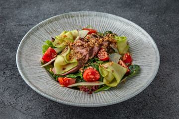 Hearty salad with duck fillet, tomatoes, zucchini and spinach. Diet food. Ready menu for the restaurant. Neutral gray blue textured background