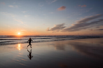 young girl running and jumping with happiness on the beach at sunset