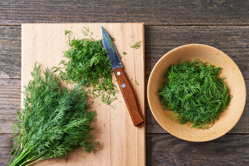 Fresh chopped green dill leaves on a cutting board, top view.