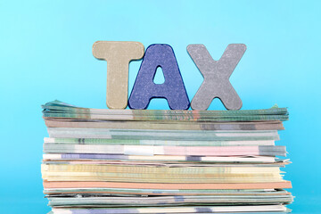 A stack of various banknotes and three-dimensional letters composed of TAX