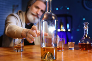 Senior man with bottle of drink at table in bar