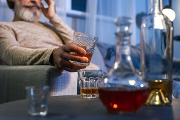 Senior man with glass of drink late in evening at home, closeup