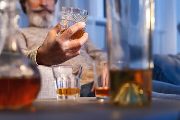 Senior man with glass of drink late in evening at home, closeup