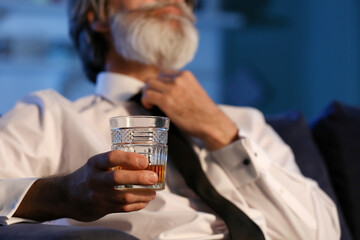 Senior man with glass of drink late in evening at home, closeup