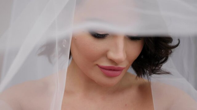 Close-up portrait of a bride in a dress with a veil that covers her head.