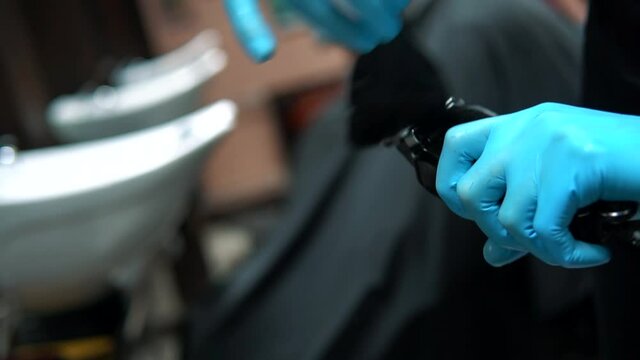 Brushing electric hair clippers. Hairdresser prepare hair machine. Barber clean black shaving machine in a barbershop. Hairdresser tools maf hands in a rubber gloves. Post pandemic enviroment.