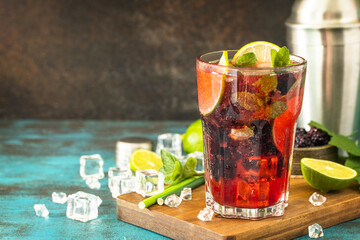 Summer refreshing drink with blackberry, mint, lime and ice, mojito or blackberry soda, on a dark stone table. Copy space.