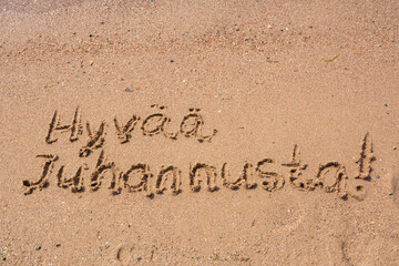 Finnish words Hyvaa Juhannusta (Happy Midsummer) handwritten on a sandy beach