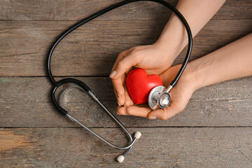 Female hands with red heart and stethoscope on wooden background