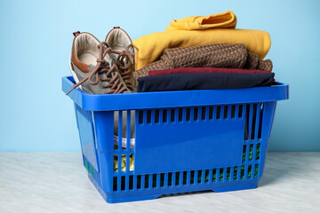 Shopping basket with shoes and clothes on table near color wall