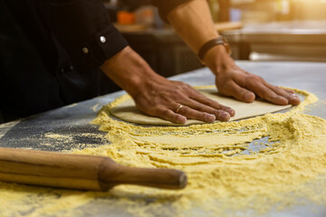 Professional chef cooking in the kitchen restaurant at the hotel, preparing dinner. A cook in an apron makes a pizza. man rolls out pizza dough