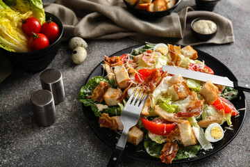 Plate with tasty Caesar salad and ingredients on grunge background