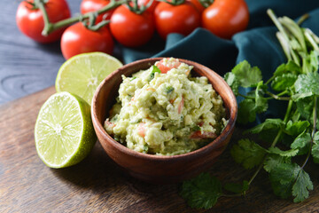 Bowl with tasty guacamole, tomato and lime on color wooden background, closeup