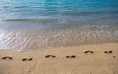 Sandy tropical beach with sea waves. Foot steps on the shore. Footp rints in the sand at sunset.