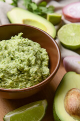 Bowl with tasty guacamole, avocado and lime on table, closeup