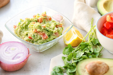 Bowl with tasty guacamole, lemon and onion on light background, closeup