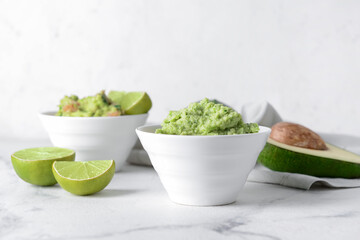 Bowls with tasty guacamole, avocado and lime on light background, closeup