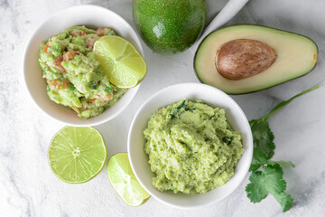 Bowls with tasty guacamole, avocado and lime on light background