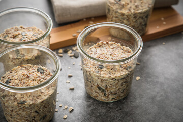 Brotteig von Vollkorn Brot mit Kürbiskernen, Haferflocken, Sonnenblumenkernen, Chia und Leinsaat roh im Glas für Einkochen und Vorrat auf Leinentuch, Holzbrett und Marmor Hintergrund dunkel