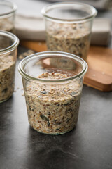 Brotteig von Vollkorn Brot mit Kürbiskernen, Haferflocken, Sonnenblumenkernen, Chia und Leinsaat roh im Glas für Einkochen und Vorrat auf Leinentuch, Holzbrett und Marmor Hintergrund dunkel