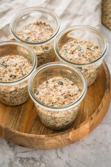 Brotteig von Vollkorn Brot mit Kürbiskernen, Haferflocken, Sonnenblumenkernen, Chia und Leinsaat roh im Glas für Einkochen und Vorrat auf Leinentuch, Holzbrett und Marmor Hintergrund hell