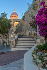  Scenic view of stairs leading to st nikolas church with a blooming bougainvillea aside and an extrerior of a traditional cafe , in ermoupolis Syros Greece