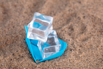 Fototapeta na wymiar Paper boat with ice cubes on the sand