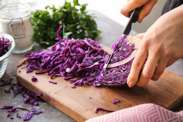 Woman cutting fresh purple cabbage on table, closeup