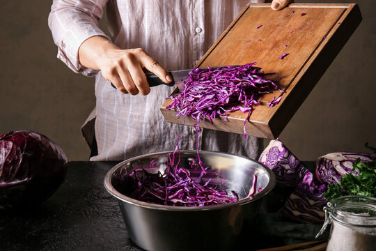 Woman cutting fresh purple cabbage on dark table