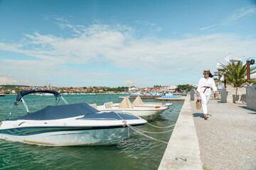 Fototapeta premium young pretty woman in white summer clothing walking by yachts dock