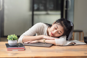 Front view of Asian woman tired of working sleeping at office desk.