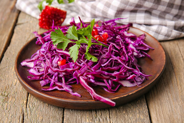 Obraz na płótnie Canvas Plate with cut fresh purple cabbage and pomegranate on wooden background, closeup