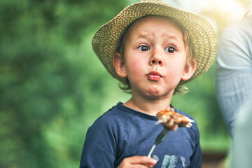 Surprised little boy eats grilled chicken wing in park - 444678827