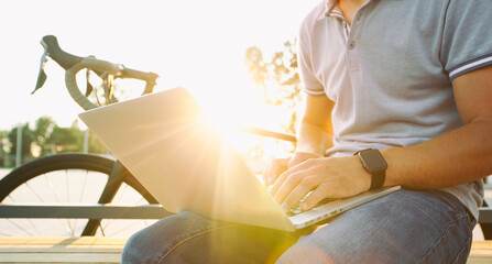 Young man working on laptop a while sitting on the bench near his bicycle