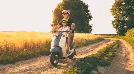 The father and son riding together through the field by pathway on the retro scooter