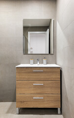 Modern refurbished bathroom in minimalist style with gray tiled walls, mirror and wooden drawers...