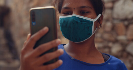 Shallow focus of an Indian girl wearing a face mask and taking a picture on her smartphone