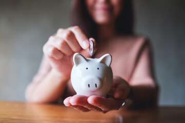 Closeup image of a woman putting coins into piggy bank for saving money concept