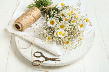 Fototapeta na wymiar Bouquet of beautiful chamomile flowers, scissors and rope on light wooden background