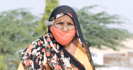 Old Indian woman wearing a traditional sari an face mask- new normal concept